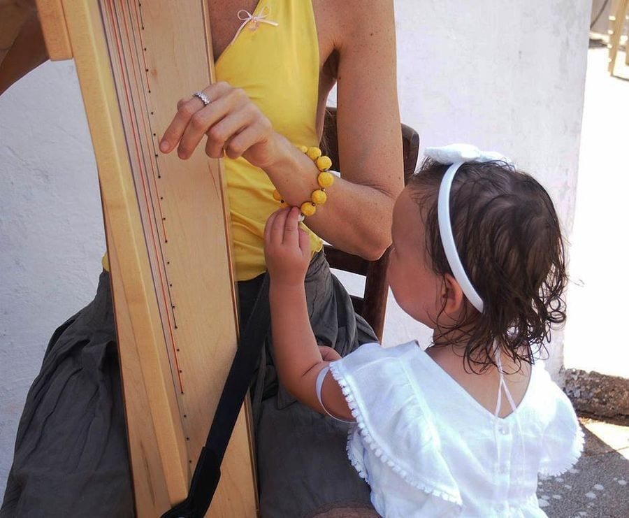 little girl watching and touching a bracelet from yellow beads of the woman playing harp at Korogonas Ark